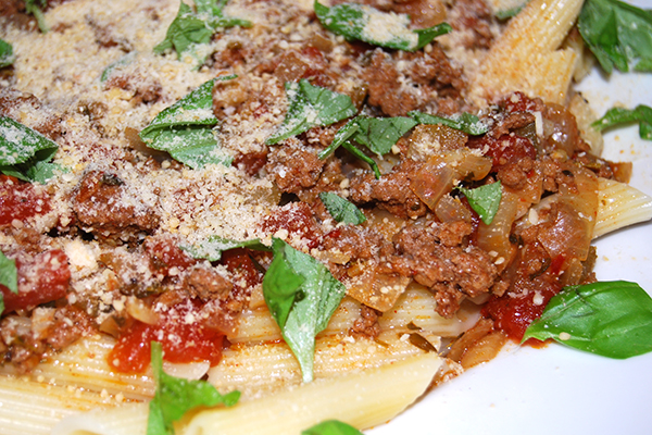 Penne Rigate mit Hackfleischsauce, mit Parmesankäse und Basilikumblättern garniert