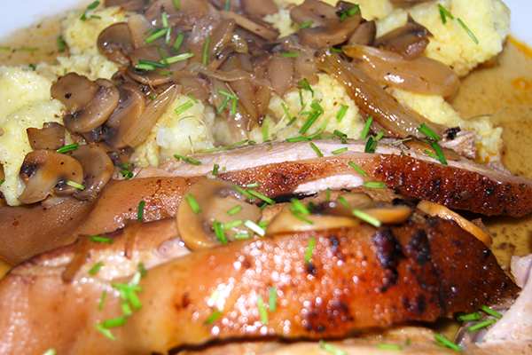Spanferkelscheiben mit Kartoffelklösen in Pilzsauce, mit Schnittlauch garniert